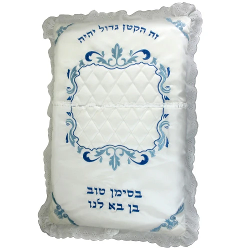The pillow Rabbi Glantz brings to the bris — embroidered with זה הקטן גדול יהיה (this small one will become great) and בסימן טוב בן בא לנו (with a good sign, a son has come to us)